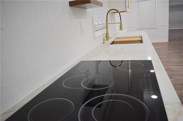 interior details featuring light stone countertops, black electric stovetop, dark wood-type flooring, and sink