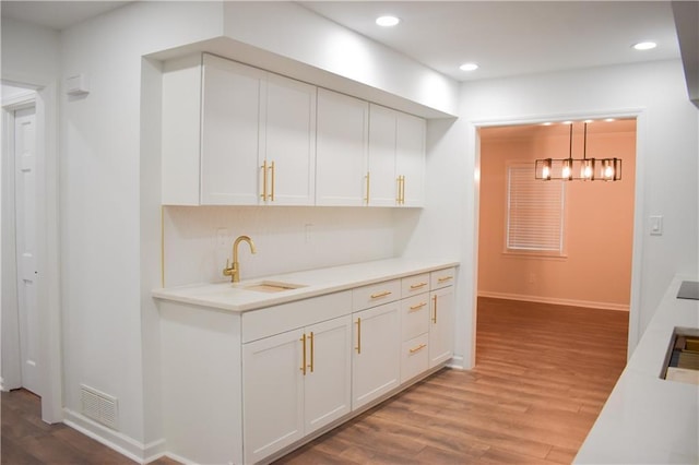 bar featuring pendant lighting, white cabinets, light wood-type flooring, and sink