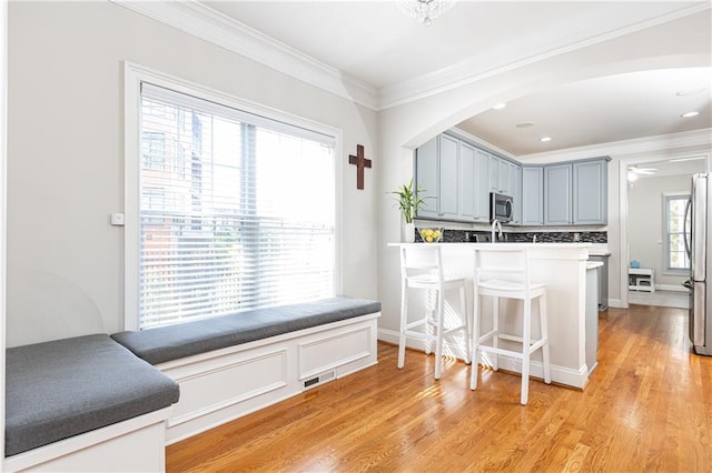 kitchen featuring appliances with stainless steel finishes, ornamental molding, a kitchen bar, light wood-type flooring, and arched walkways
