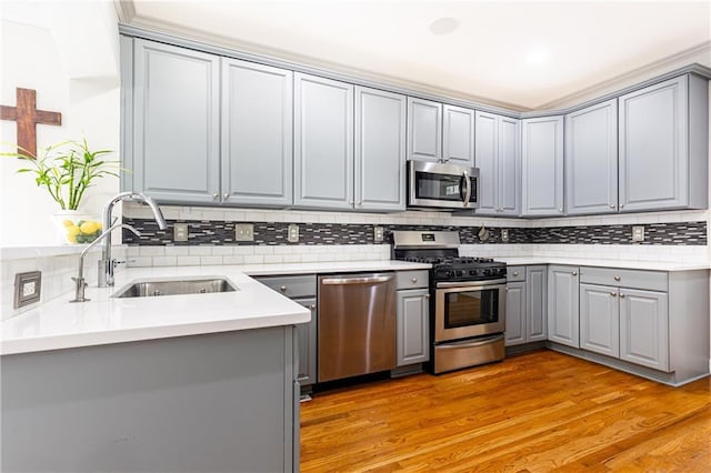 kitchen featuring gray cabinetry, appliances with stainless steel finishes, a sink, backsplash, and light wood-style flooring
