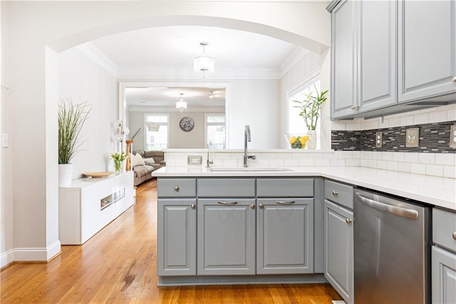 kitchen featuring gray cabinets, stainless steel dishwasher, a sink, arched walkways, and a peninsula