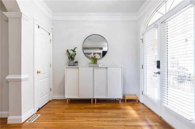 foyer featuring light wood-style floors, ornamental molding, ornate columns, and baseboards