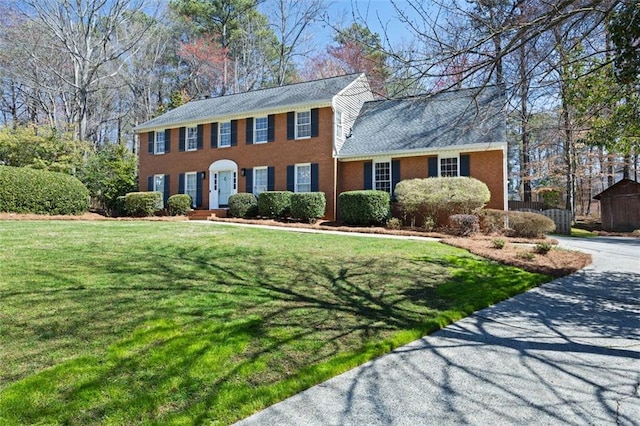 colonial house featuring a front yard, brick siding, and driveway