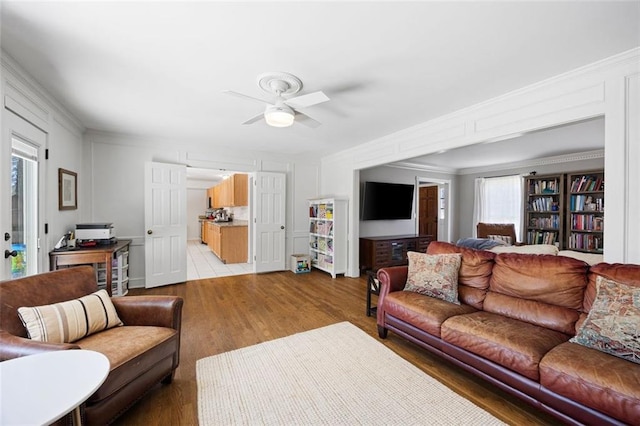 living room with light wood finished floors, crown molding, and ceiling fan