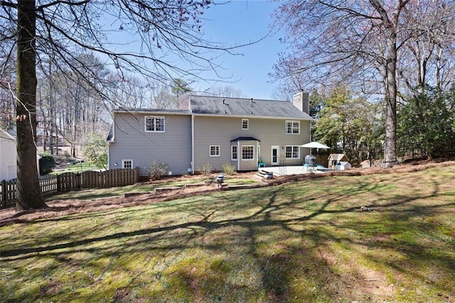 rear view of property with a lawn, a chimney, a patio, and fence