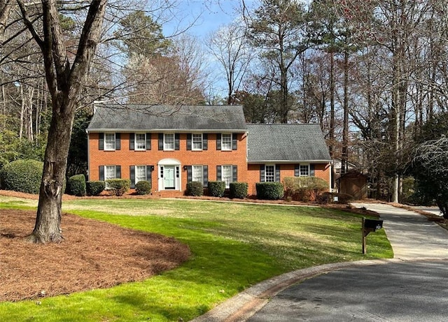 colonial inspired home featuring brick siding and a front yard