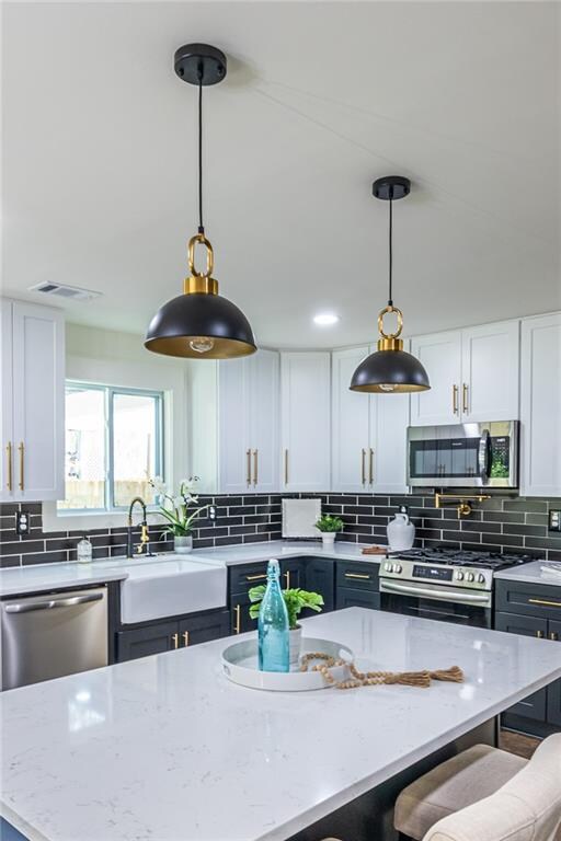 kitchen with appliances with stainless steel finishes, sink, a center island, white cabinetry, and decorative light fixtures