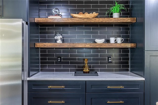 bar featuring blue cabinetry, stainless steel fridge, light stone counters, and tasteful backsplash