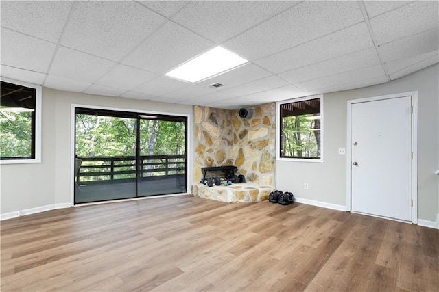 unfurnished living room with a stone fireplace, a paneled ceiling, and hardwood / wood-style flooring