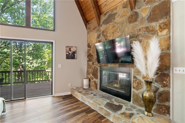 living room with a stone fireplace, plenty of natural light, wooden ceiling, and beamed ceiling