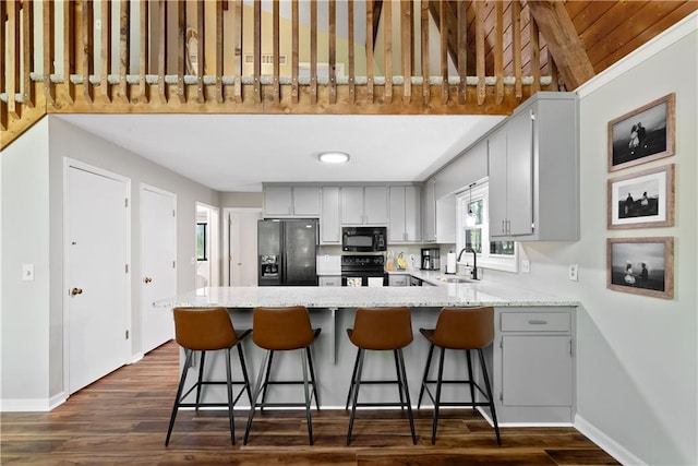 kitchen featuring sink, dark hardwood / wood-style flooring, a kitchen breakfast bar, kitchen peninsula, and black appliances