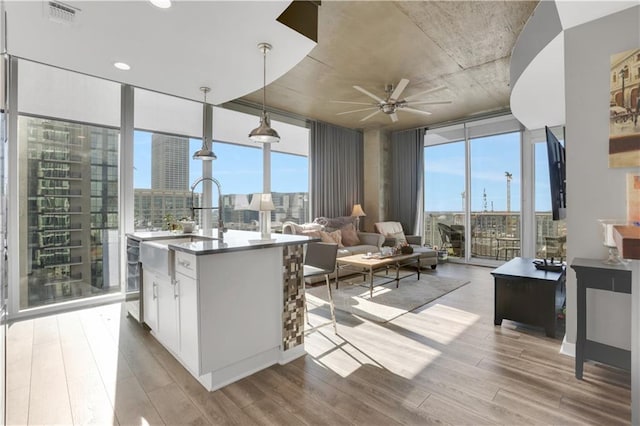 kitchen with pendant lighting, ceiling fan, a healthy amount of sunlight, a wall of windows, and white cabinetry