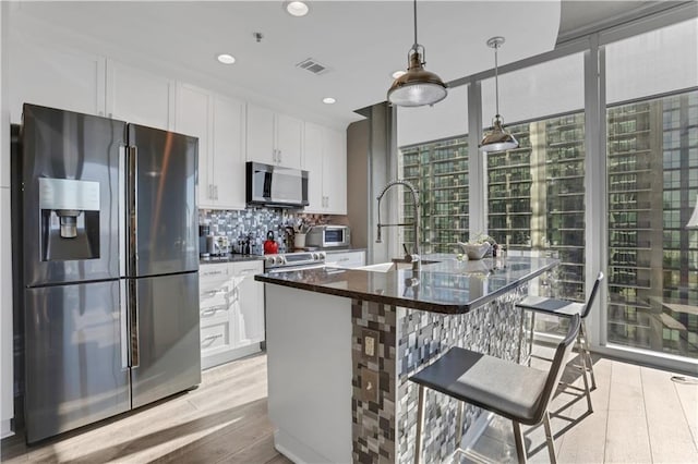 kitchen with a kitchen island with sink, white cabinets, and appliances with stainless steel finishes