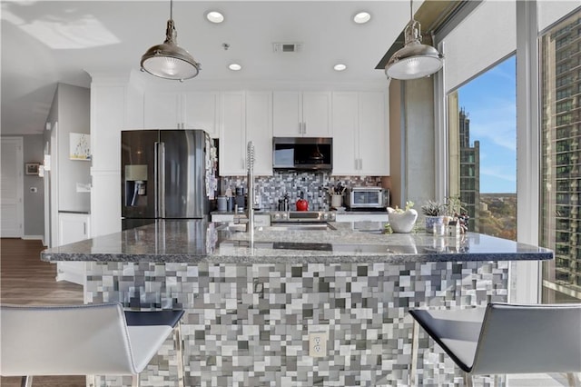 kitchen with dark stone counters, stainless steel appliances, pendant lighting, white cabinets, and a large island