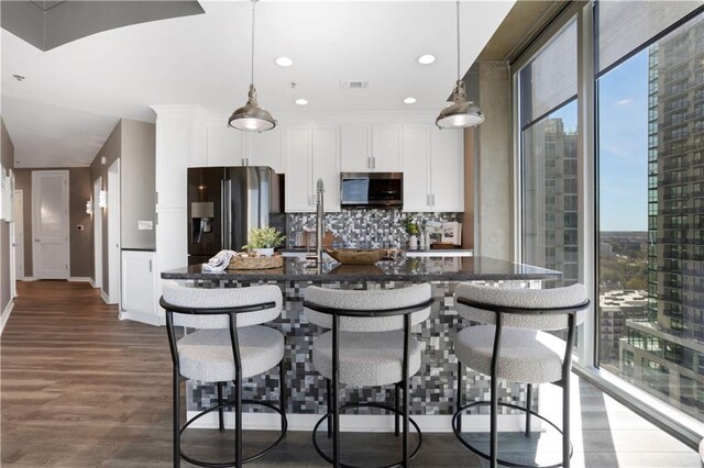 kitchen with a center island with sink, white cabinets, hanging light fixtures, and stainless steel dishwasher