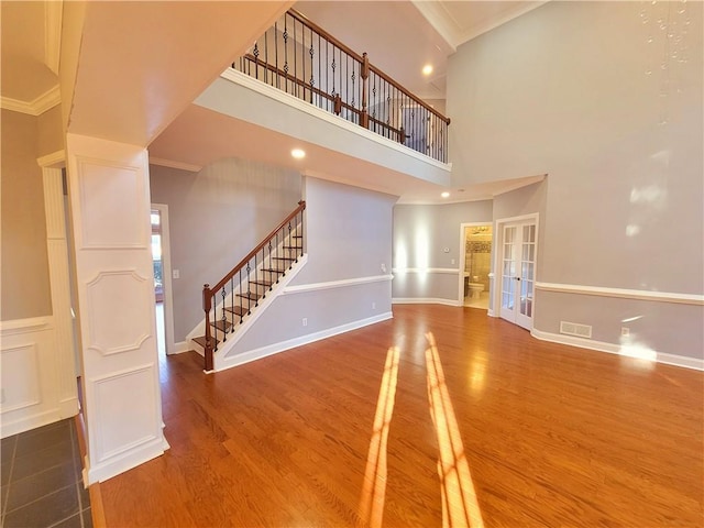 unfurnished living room with crown molding, stairs, wood finished floors, and french doors