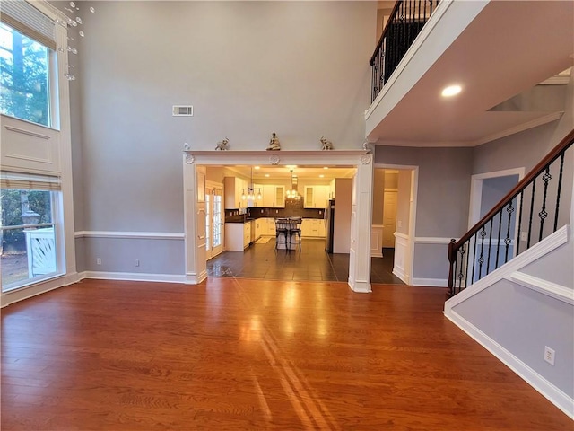 unfurnished living room with stairs, a high ceiling, dark wood finished floors, and visible vents