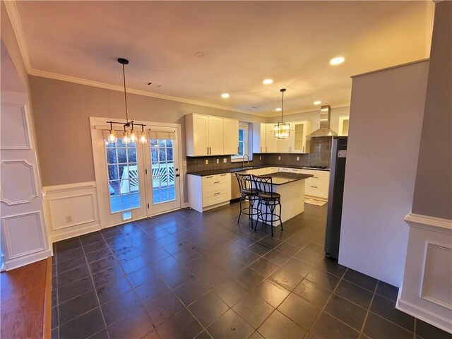 kitchen with decorative backsplash, appliances with stainless steel finishes, ornamental molding, wall chimney range hood, and white cabinetry