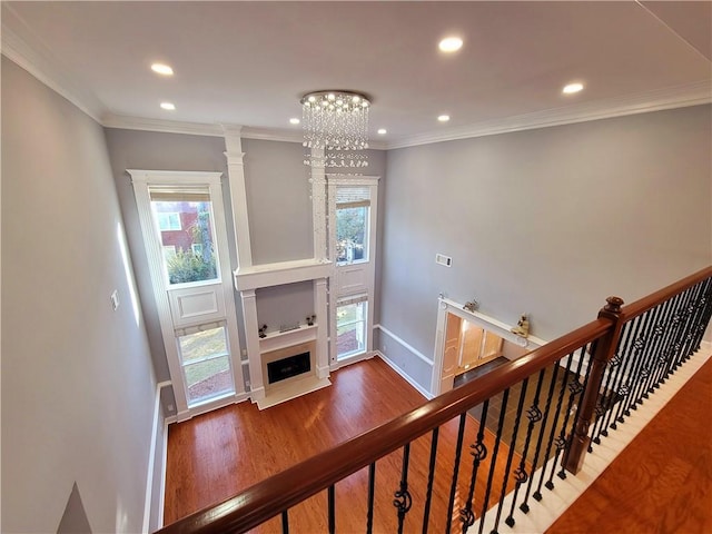 staircase with baseboards, a fireplace with flush hearth, wood finished floors, and crown molding