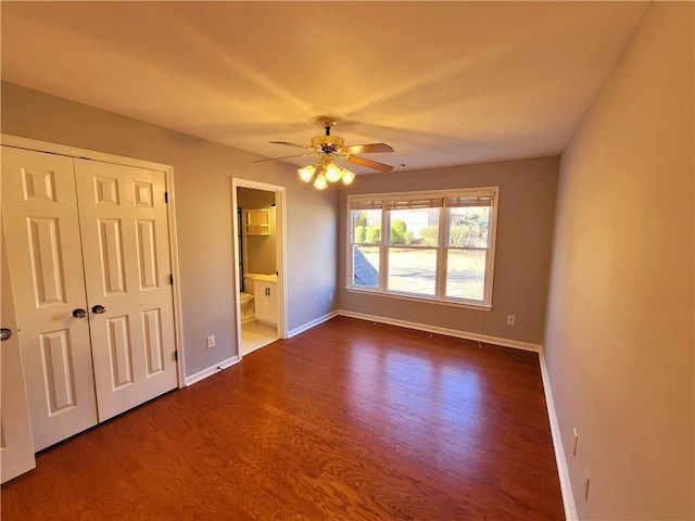 unfurnished bedroom featuring dark wood-style flooring, a closet, a ceiling fan, connected bathroom, and baseboards