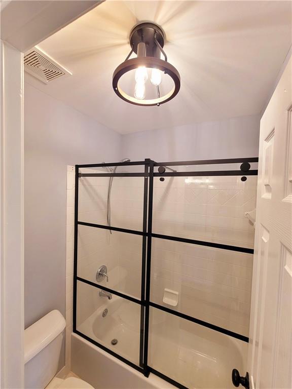 bathroom with visible vents, toilet, and bath / shower combo with glass door