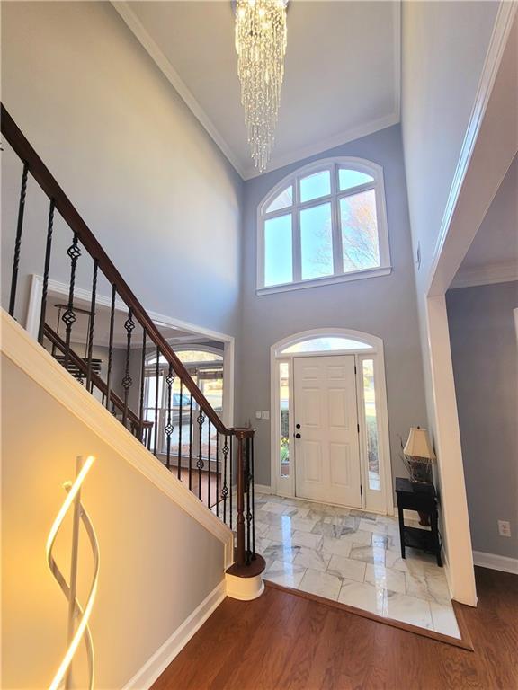 entryway with wood finished floors, a healthy amount of sunlight, ornamental molding, stairway, and an inviting chandelier