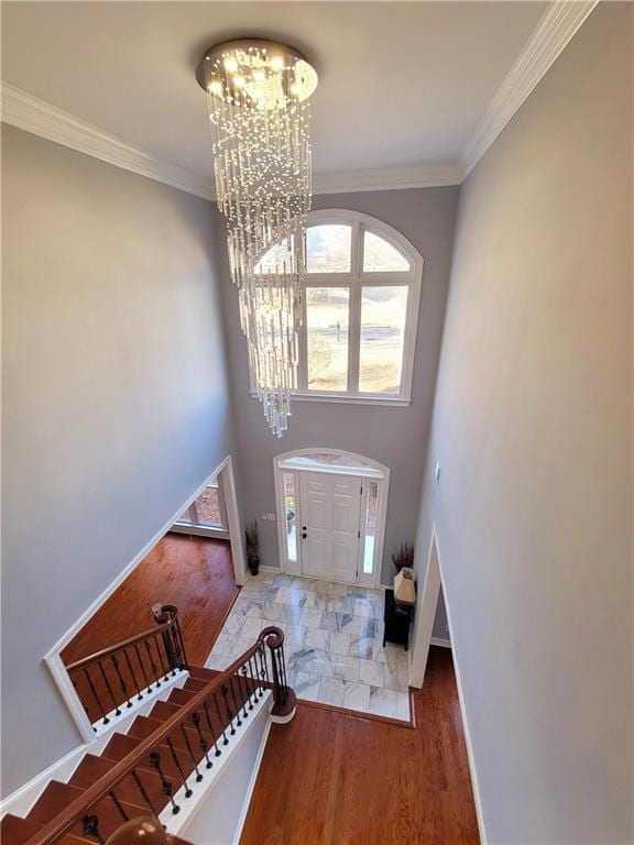 entrance foyer featuring a chandelier, wood finished floors, baseboards, stairs, and crown molding