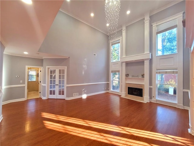 unfurnished living room with a fireplace with raised hearth, visible vents, a high ceiling, ornamental molding, and wood finished floors