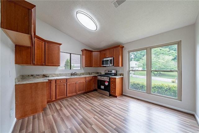 765 Martin Rd, Stone Mountain, GA 30088 - kitchen featuring stainless steel appliances, brown cabinets, light wood finished floors, a sink, and vaulted ceiling