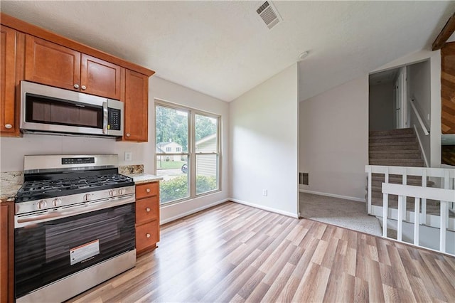 765 Martin Rd, Stone Mountain, GA 30088 - kitchen featuring appliances with stainless steel finishes, vaulted ceiling, brown cabinets, light wood-style flooring, and light stone countertops