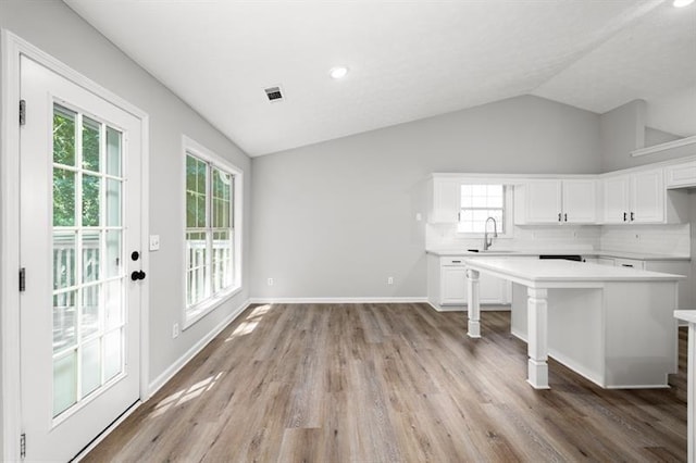 kitchen featuring vaulted ceiling, light countertops, white cabinets, a sink, and light wood-style floors