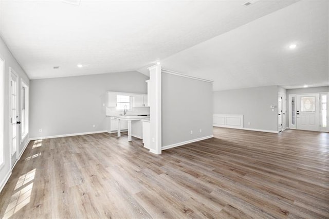 unfurnished living room with wood finished floors, lofted ceiling, plenty of natural light, baseboards, and recessed lighting
