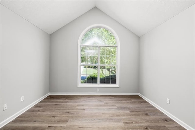 unfurnished room featuring vaulted ceiling, wood finished floors, and baseboards