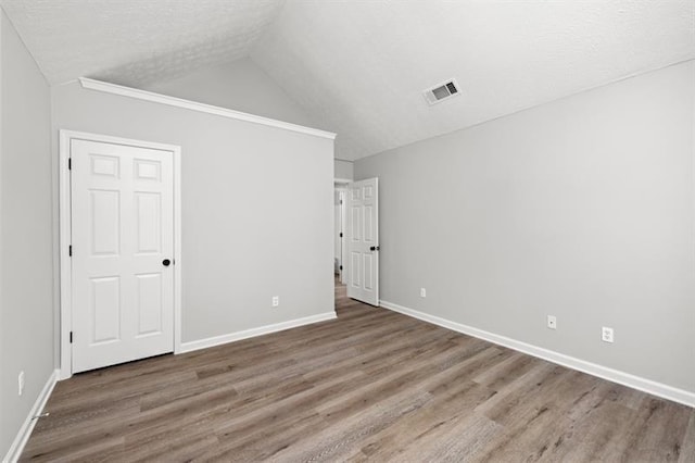 unfurnished bedroom with vaulted ceiling, wood finished floors, baseboards, and a textured ceiling