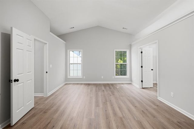 spare room with healthy amount of natural light, light wood-style flooring, and vaulted ceiling