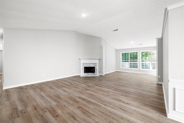 unfurnished living room featuring lofted ceiling, wood finished floors, a high end fireplace, baseboards, and recessed lighting