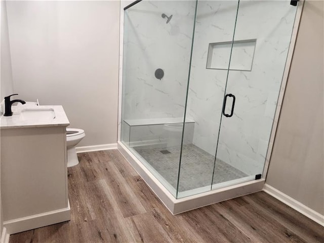 full bath featuring toilet, wood finished floors, a marble finish shower, baseboards, and vanity