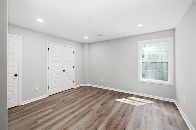 unfurnished bedroom with wood finished floors, baseboards, recessed lighting, and a closet