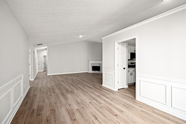 unfurnished living room featuring a high end fireplace, a decorative wall, light wood finished floors, wainscoting, and crown molding