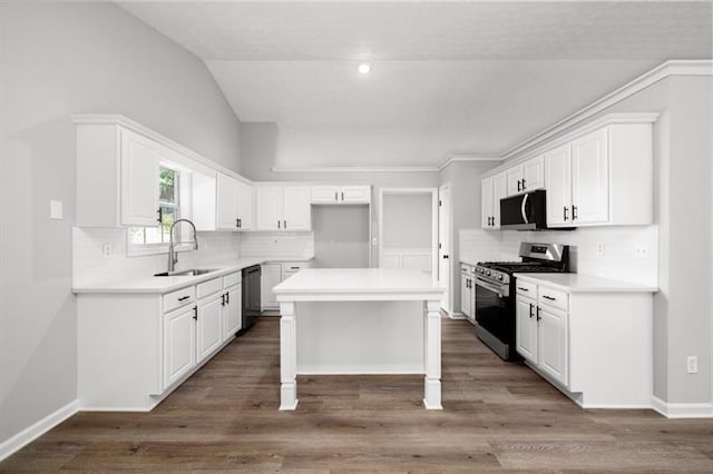 kitchen with appliances with stainless steel finishes, a sink, backsplash, white cabinetry, and a center island