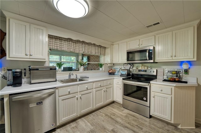 kitchen featuring stainless steel appliances, sink, light wood-type flooring, and white cabinets