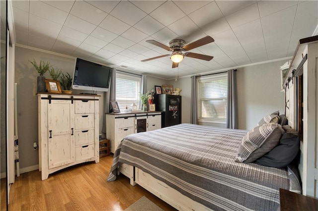 bedroom featuring a barn door, ceiling fan, ornamental molding, and light hardwood / wood-style flooring