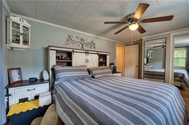 bedroom with crown molding, ceiling fan, a barn door, and hardwood / wood-style flooring