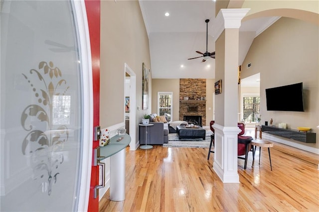 living room featuring a high ceiling, decorative columns, a stone fireplace, and ceiling fan