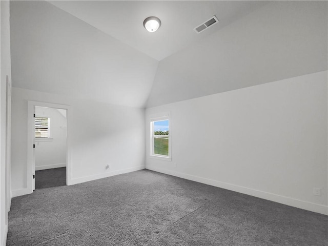 additional living space with dark carpet, visible vents, vaulted ceiling, and baseboards