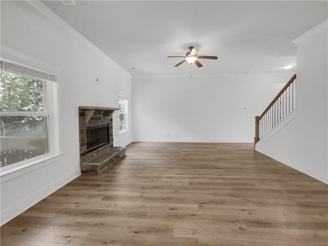 unfurnished living room with ceiling fan, a fireplace, wood finished floors, baseboards, and stairway