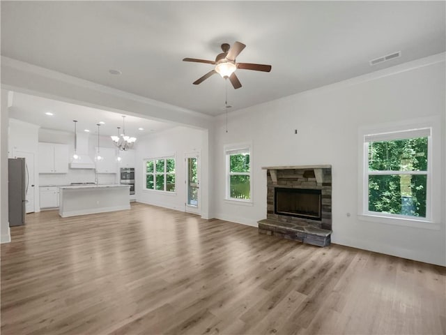 unfurnished living room featuring a stone fireplace, light wood-style flooring, recessed lighting, ceiling fan with notable chandelier, and visible vents