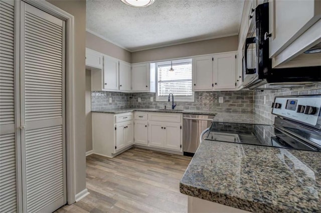 kitchen with sink, white cabinetry, light wood-type flooring, appliances with stainless steel finishes, and backsplash