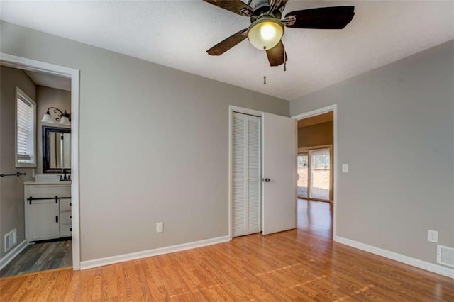 unfurnished bedroom with ensuite bath, a closet, ceiling fan, and light wood-type flooring