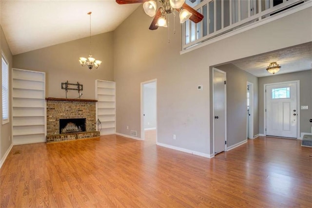 unfurnished living room featuring vaulted ceiling, wood-type flooring, a fireplace, and ceiling fan with notable chandelier